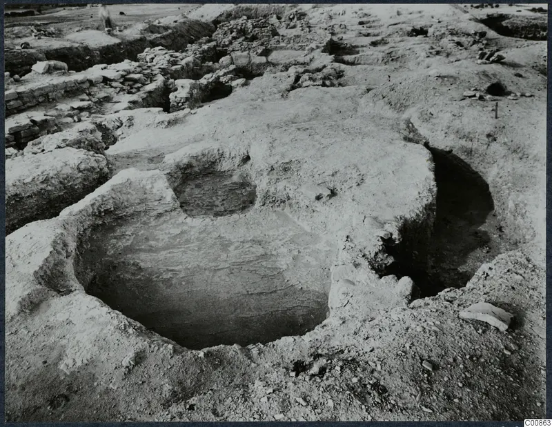 Excavation at Idalion Acropolis with a round cut in the ground, low stone walls and a person at upper left.