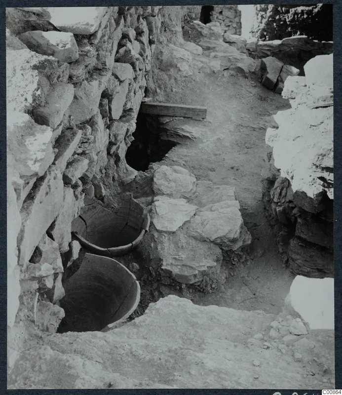 Excavation at Idalion Acropolis with two large vessels sunk into the ground beside a rough stone wall
