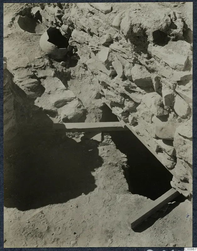 Excavation trench at Idalion Acropolis with a rough stone wall, broken pottery vessels in the soil and wooden boards laid across the cut