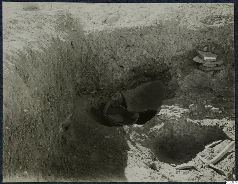 Excavation trench at Idalion Acropolis with a broken pottery vessel lying in a pit and a stack of flat stones