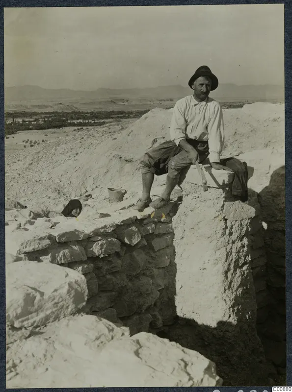 Panajiotis sitting on a stone wall at the excavation at Idalion, with hills and a valley behind.
