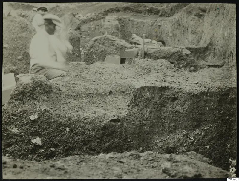 Excavation at Plakes, Lapithos, with two people among trench walls and a wooden box.