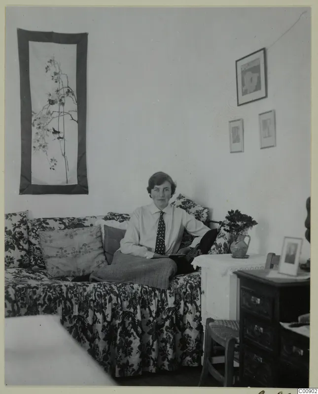Vivi Gjerstad seated on a floral sofa in a room with wall hangings and framed pictures, Nicosia