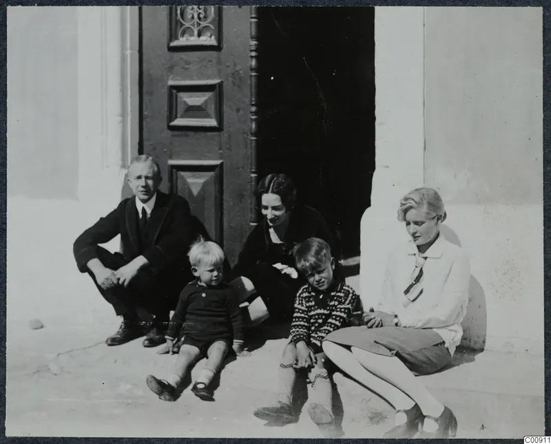 Five people, two adults and three children, sitting on a stone step in front of a dark wooden door.