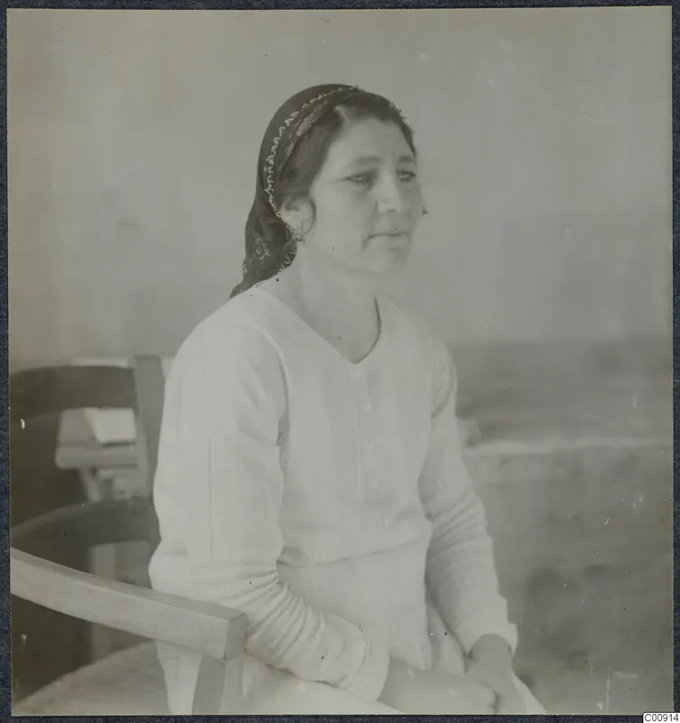 Portrait of Maria in Nicosia, a woman in a headscarf and light blouse seated in a wooden chair.
