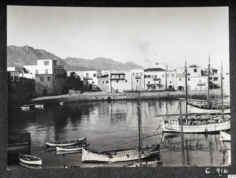 Kyrenia harbour with whitewashed buildings along the quay, moored boats on the water and mountains behind.