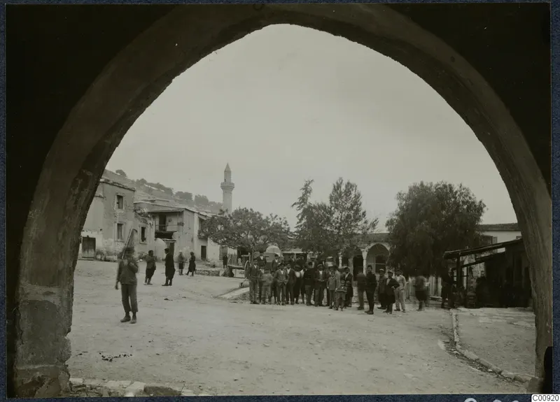View through a large arch over the village square at Kalavassos, with a minaret and a group of men standing in the street