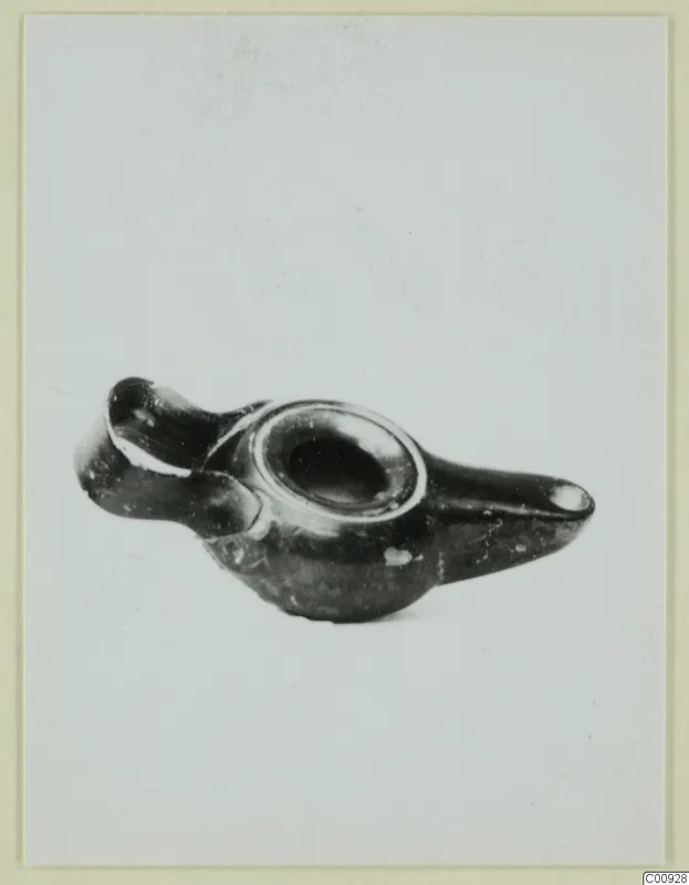 Black-glazed lamp with a central filling hole, a broken nozzle at left and a long handle at right, on a pale background.