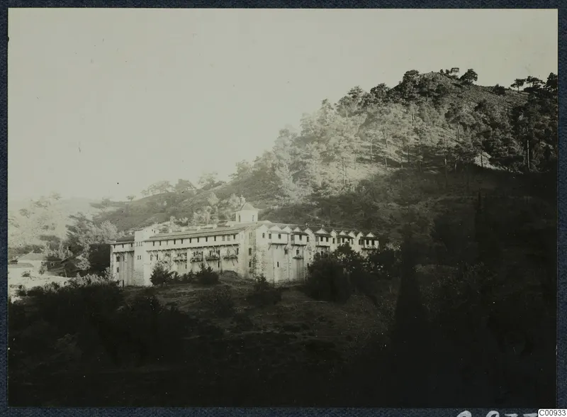 Machairas monastery, a long whitish multi-storey building with a small tower on a wooded hillside, seen from the west