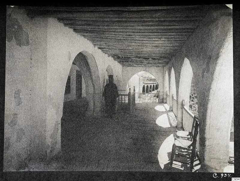 Arcaded walkway in the monastery courtyard at Lambousa, with a man in a long dark robe walking along it