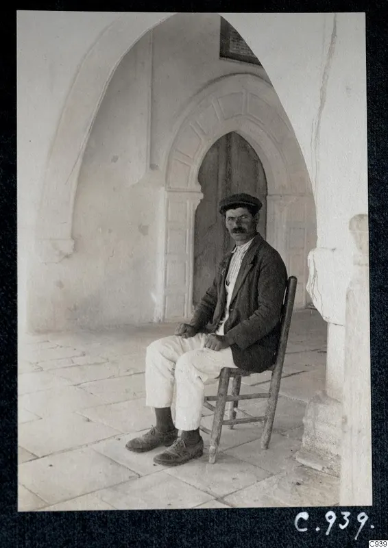 Solon seated on a wooden chair in a vaulted monastery corridor