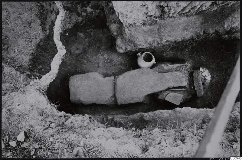 Excavated cut at Lapithos Tomb 422 with two long stone slabs laid over the fill and a small jug beside them.