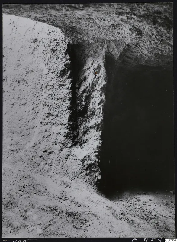 Tomb 422 at Lapithos during excavation, showing a cut rock face beside a dark tomb chamber opening