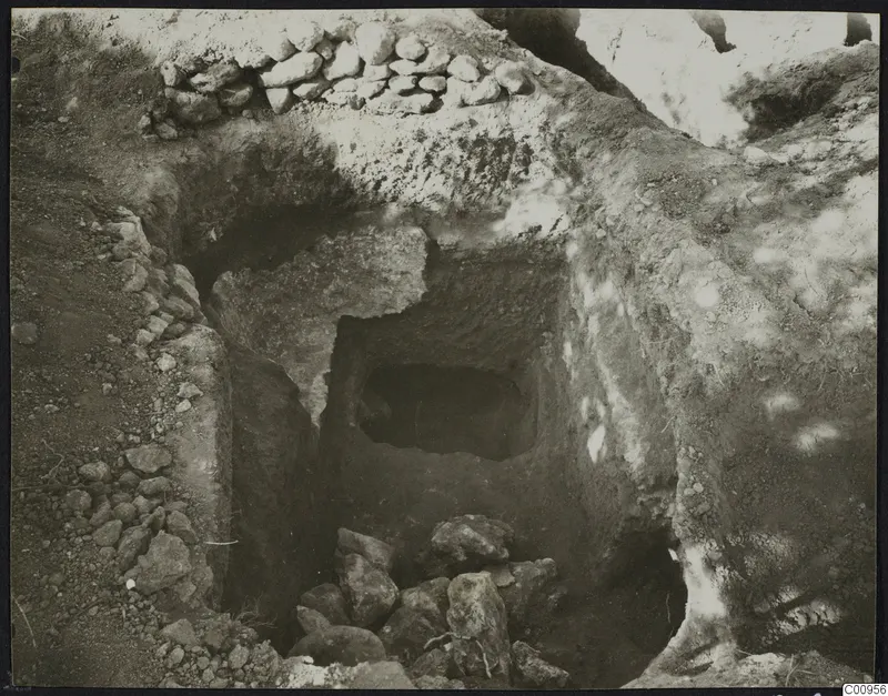 Tomb 427 at Lapithos during excavation, showing the tomb chamber opening behind a sloping cut with loose stones on the floor