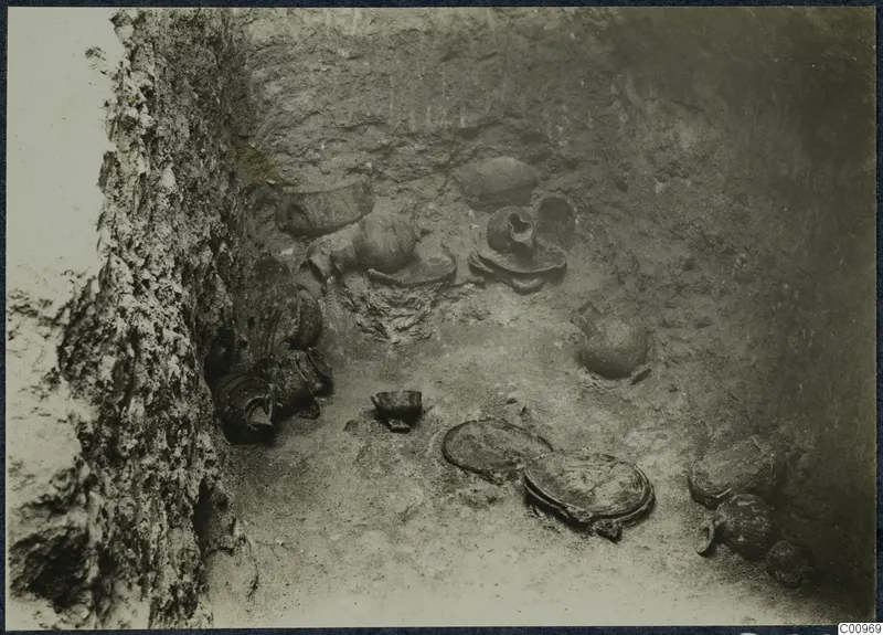Pottery vessels lying in situ on the floor of an excavated pit, with a rock-cut wall on the left.