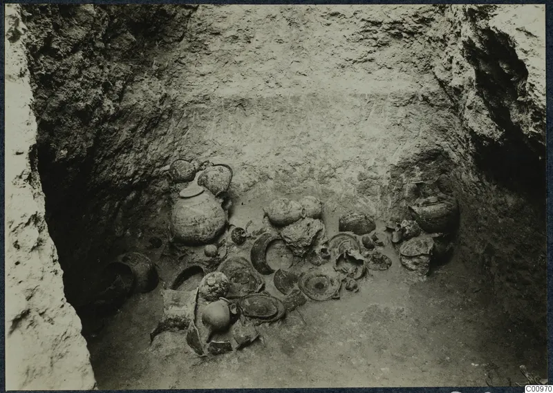 Pottery vessels and sherds lying on the floor of a cut pit at Idalion, seen from above.