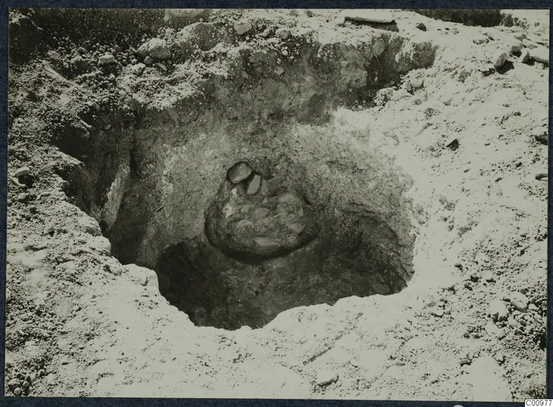 Excavation cut at Idalion with a rounded mass of stones and earth in its centre, surrounded by loose stones and pale soil.