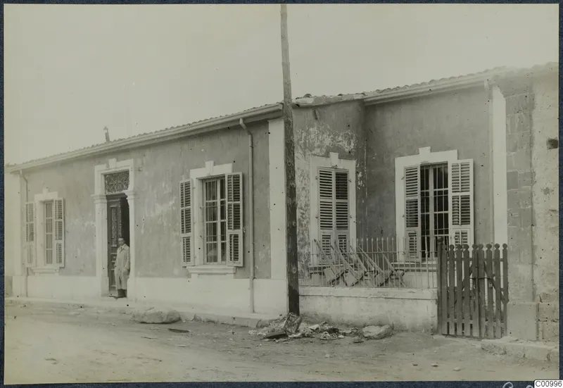 A single-storey rendered building with shuttered windows and a man standing in the doorway, Nicosia