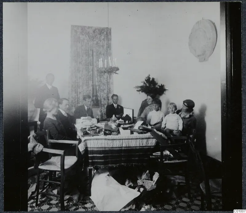 Christmas Eve 1928 gathering around a table of presents, with about ten people and two children in a room