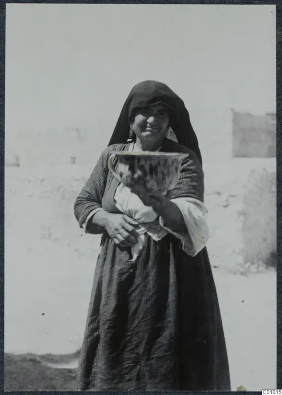 Smiling woman in a dark headscarf and dress holding a large bowl with dark streaked glaze, Karpas peninsula