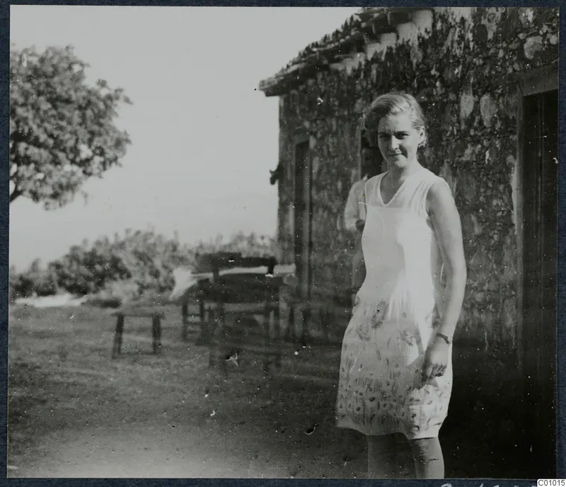 Gudrun Atterman standing outside a stone house at Vouni, with a tree and open ground behind her.