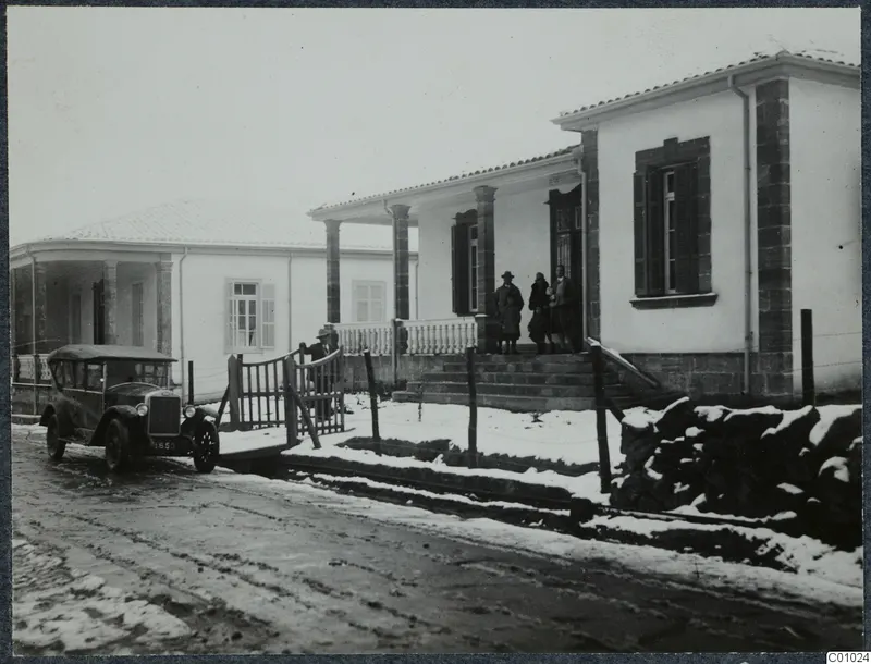 The Swedish house in Nicosia, a white building with a columned veranda, people on its steps and an old car in snow.