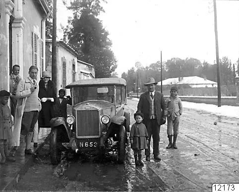 Street in Nicosia with an old car and a group of adults and children standing beside it, patches of snow on the ground