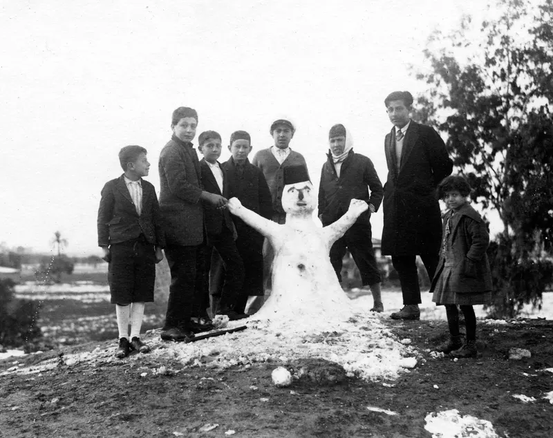 Snowman with a group of eight children and a young man standing around it in Nicosia