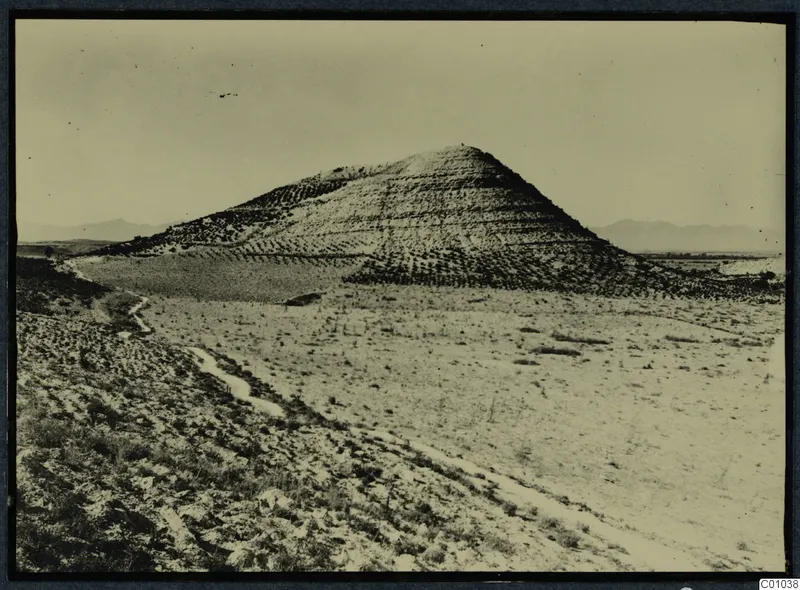 Steep conical hill rising from open dry land at Idalion, with terraced slopes and a dirt track below.