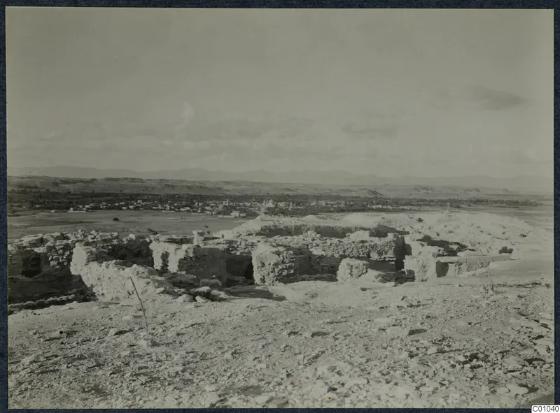 Ruined stone walls on a stony hilltop at Idalion, with a town and hills in the distance