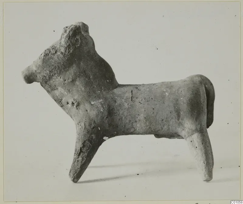 Terracotta figurine of a standing bull facing left, shown in side profile against a pale background