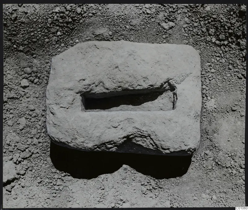 Rectangular pale stone block with a rectangular hollow in its top, lying on loose soil at Tomb 422, Lapithos Kastros