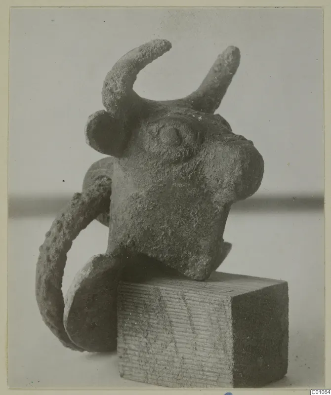 Bronze bull-head object with curved horns and a loop at one side, set on a wooden block