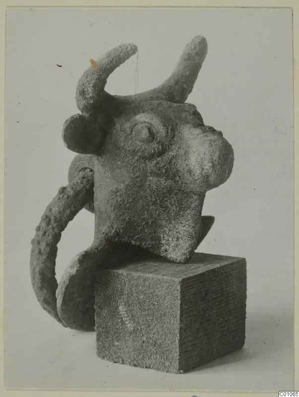 Bronze bull's head object with upturned horns and a curved loop, set on a square stone block