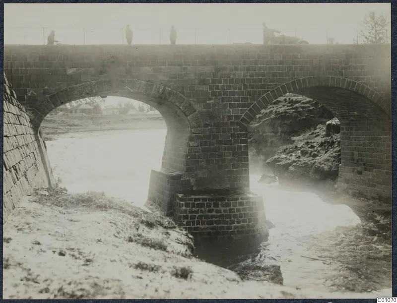 Two-arched stone bridge over a stream bed, with four people on the deck above, at Nicosia.