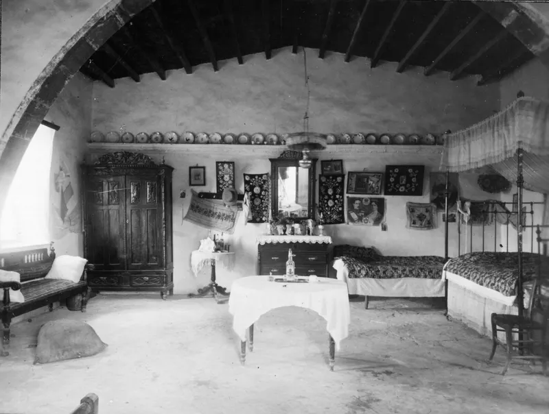 Interior of Panagiotis' house at Idalion, with beds, a round table and a mirror on the wall
