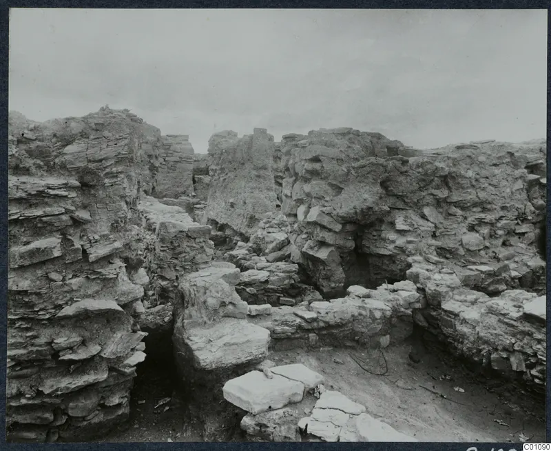 Overall view of grid square K 4 at Idalion, looking south, showing excavated walls and flat stone slabs.
