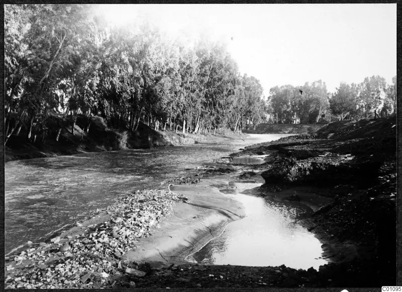 River channel in Nicosia lined with stones and tall trees on the left bank.