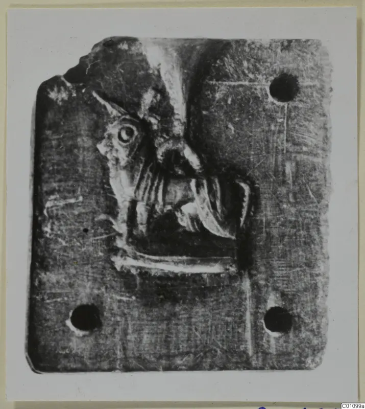 Flat rectangular stone with a relief carving of a head in profile and three pierced holes.