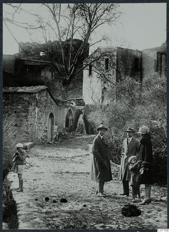 Street in Kythrea with stone buildings, a bare tree and five people standing on the cobbled lane