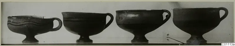Four footed bowls with single loop handles standing in a row, photographed from the side.