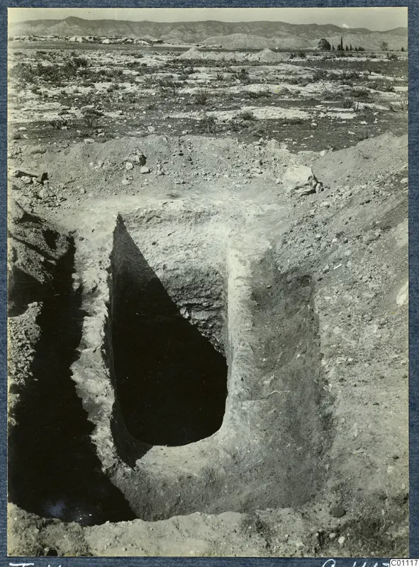 Tomb 11 at Milia during excavation: the open tomb chamber cut into pale soil and stones, with hills behind