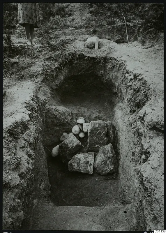 Dromos of Tomb 4 at Marion, an excavated cut with a heap of stones, with a person's legs at the top edge.