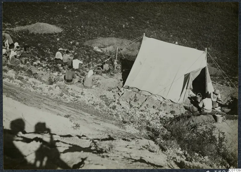 People sitting near a large white tent with baskets and buckets on a slope at Marion