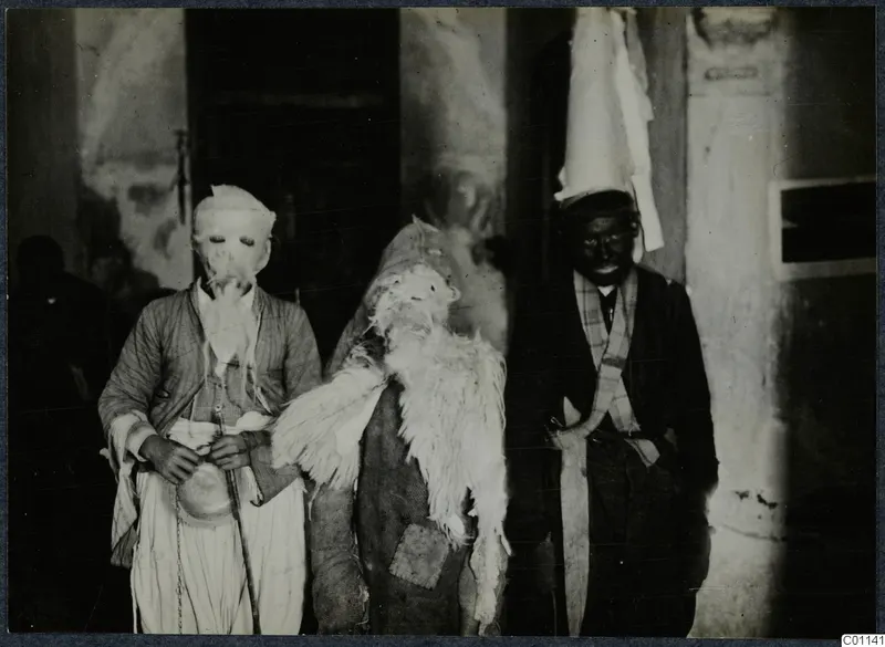 Three people in animal-skin and mask costumes stand together outside a doorway, last day of the carnival at Marion.