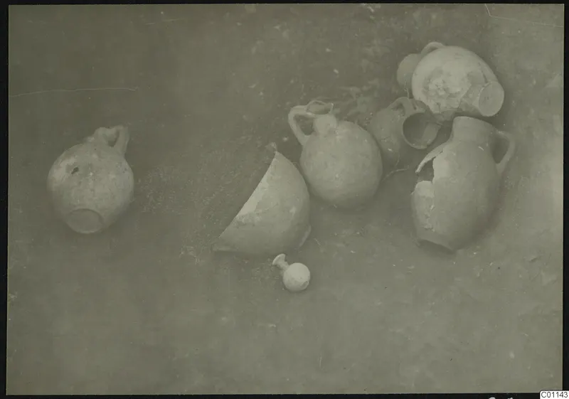 Several clay jugs and jars lying on the ground during excavation at Marion, Tomb 4.