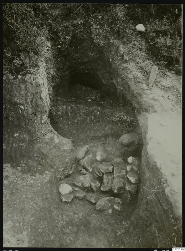 Tomb 8 at Marion during excavation, with a dromos cut into the earth and a heap of stones in the foreground.