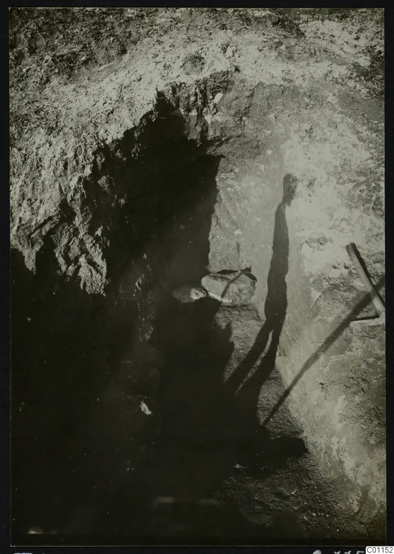 Excavation trench at Marion with a tool at the right edge and a long shadow falling across the cut wall.