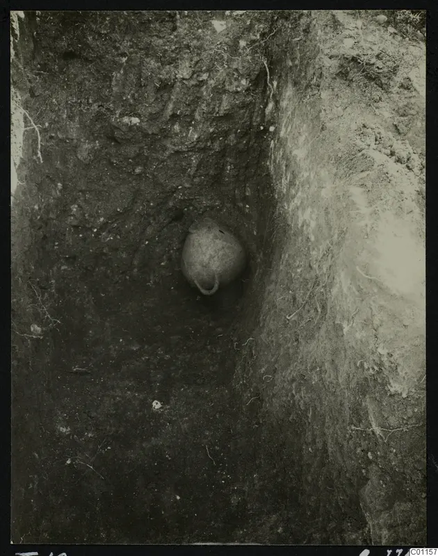 Tomb 10 at Marion during excavation, with a rounded vessel set into the soil of a narrow cut.