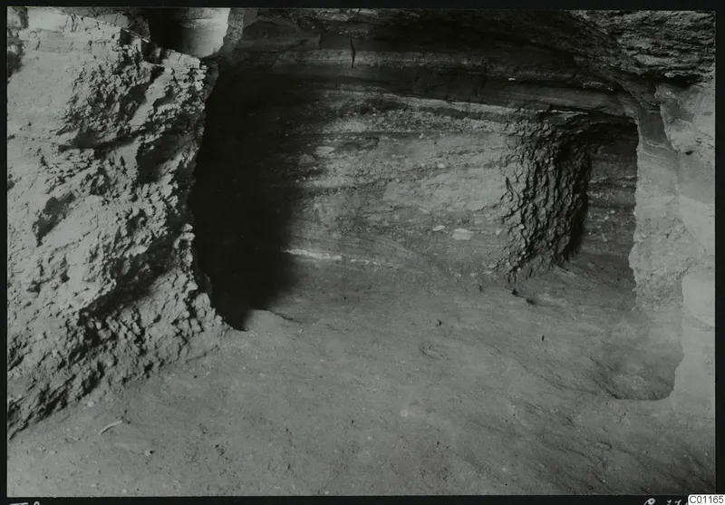 Rock-cut tomb passage at Marion during excavation, with layered rock walls and a sandy floor.